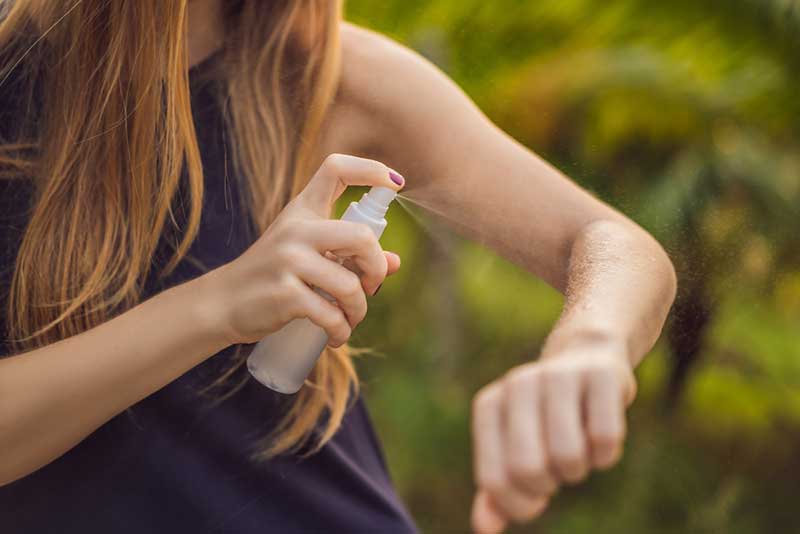 Woman spraying bug repellent on her arm